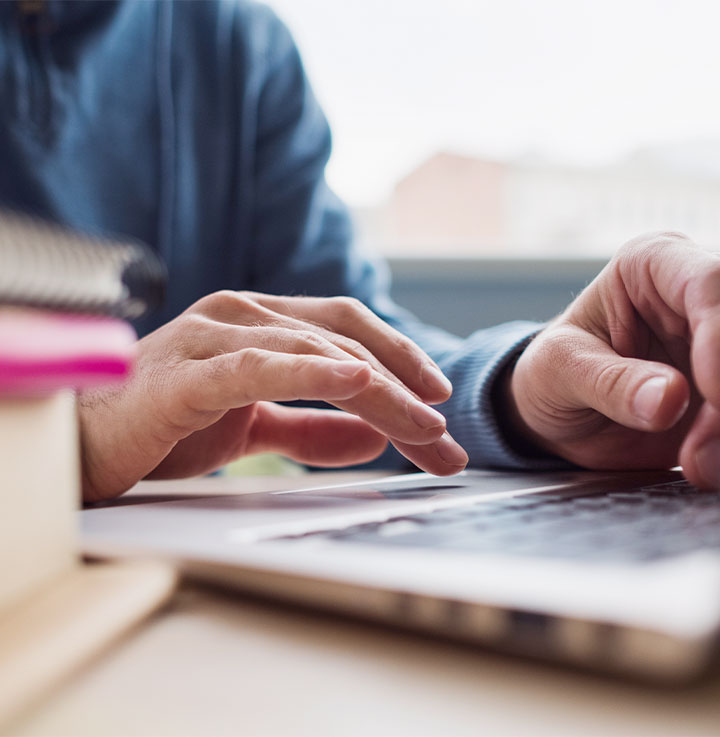 Κοντινό πλάνο χεριών που χρησιμοποιούν το trackpad και το πληκτρολόγιο ενός φορητού υπολογιστή.